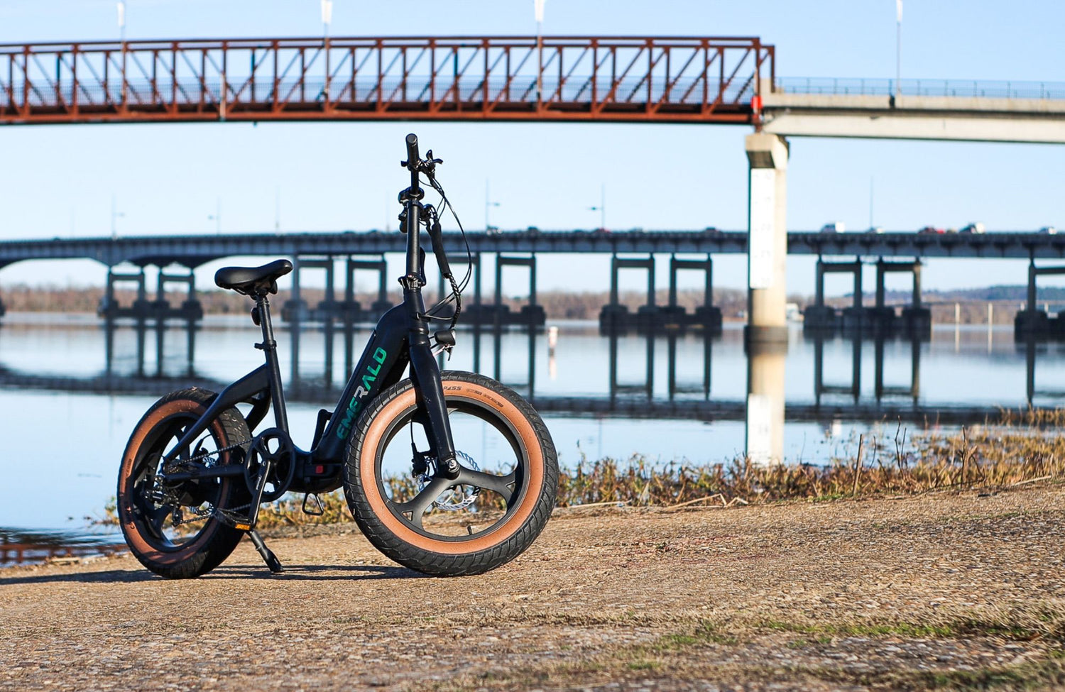 Emerald ebike parked on a riverbank with a bridge in the background